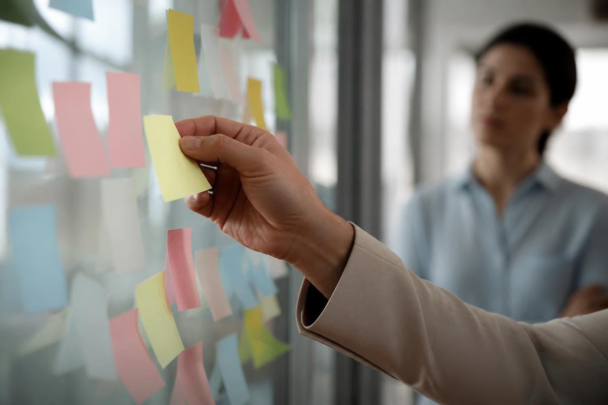 Mão colando um post-it em uma parede de vidro com o mapa de um processo