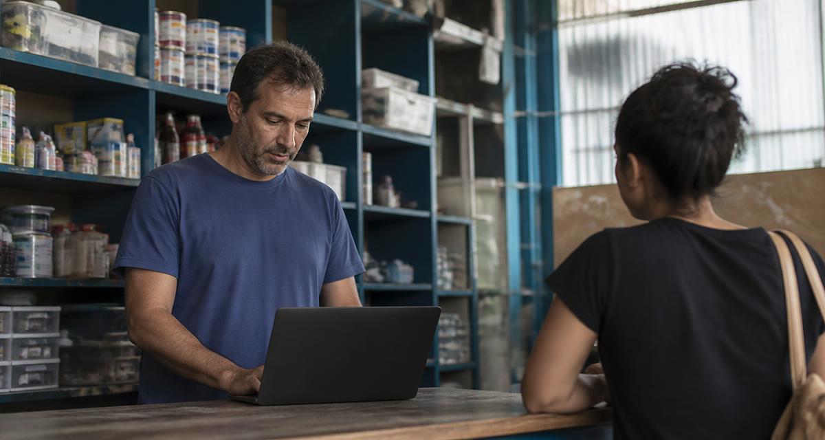 Dono de pequeno negócio usando um notebook no balcão da loja enquanto atende uma cliente
