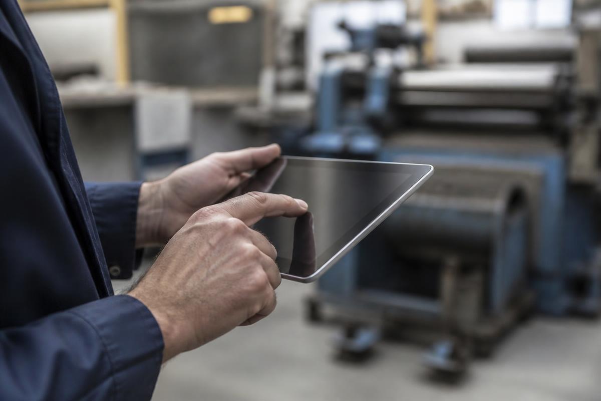 Operador usando um tablet no chão de fábrica, com máquinas ao fundo